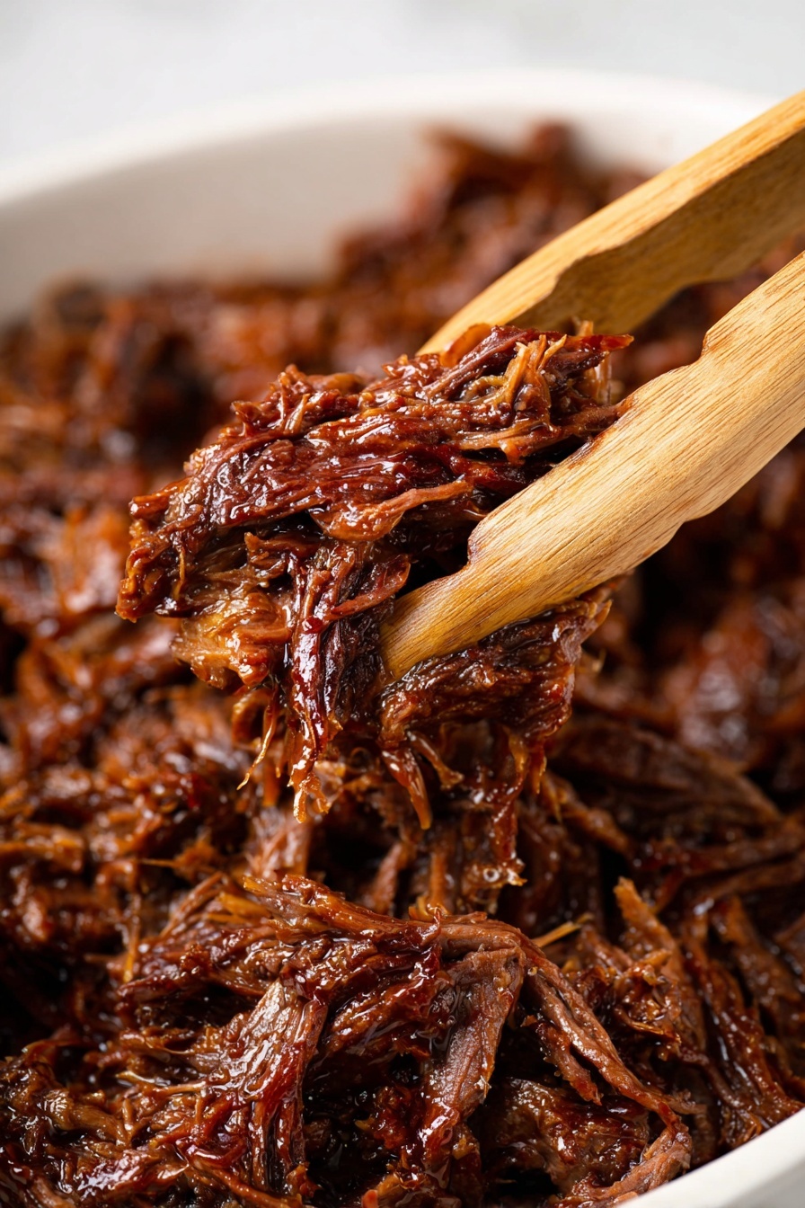 The image shows a close-up of moist, shredded dark brown meat held by wooden tongs. The meat looks tender and shiny with visible fibers and a slightly sticky texture. In the background, more shredded meat fills the white container, with rich, deep brown colors and some hints of red. The scene is set on a white marbled surface, focusing on the texture and moisture of the meat. Photo taken with an iphone --ar 2:3 --v 7