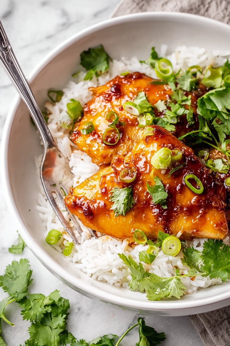 A white bowl holds two pieces of golden glazed chicken thighs layered on a bed of fluffy white rice. The chicken is shiny with a sticky dark brown sauce that has a reddish tint, and it is topped with chopped green onions and fresh cilantro leaves. The rice looks soft and slightly sticky, filling the bottom of the bowl evenly. A silver fork rests inside the bowl, touching the rice near the chicken. The background is a white marbled surface with some green cilantro leaves scattered around. Photo taken with an iphone --ar 2:3 --v 7