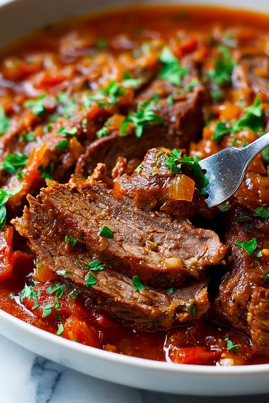 The image shows a close-up of tender beef slices in a thick, rich tomato-based sauce with visible pieces of cooked onions and small bits of carrots. The beef appears soft and juicy, with some slices showing grain and texture. The sauce is deep red-orange and coats the meat well, sprinkled with fresh chopped green herbs. A silver fork is inserted into one sliced piece of beef, lifting it slightly. The dish is served in a white pan resting on a white marbled surface. The lighting highlights the moist texture of the meat and the glossy sauce photo taken with an iphone --ar 2:3 --v 7