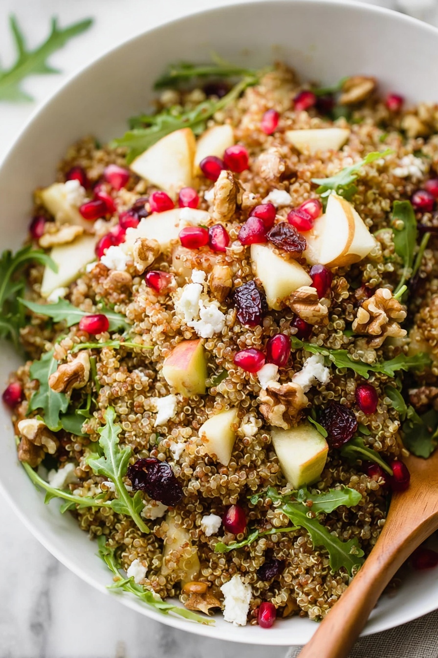 A white bowl filled with a colorful quinoa salad sits on a white marbled surface, topped with bright red pomegranate seeds, small green arugula leaves, chopped light yellow apple pieces with red skin, crumbled white goat cheese, and scattered dark dried cranberries and walnuts. A wooden spoon lies inside the bowl on the right side, slightly covered by the salad. Around the bowl, there are some loose quinoa grains, arugula leaves, and pomegranate seeds, with a few pieces of pomegranate fruit near the top left corner of the image. Photo taken with an iphone --ar 2:3 --v 7