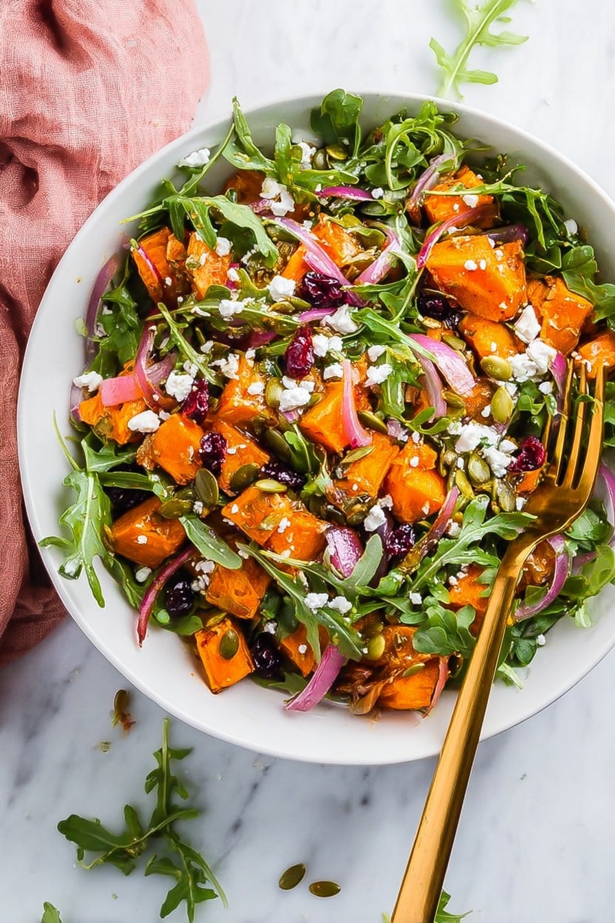 A white bowl holds a colorful salad with three main layers. The bottom layer is fresh green arugula leaves, spread evenly. On top, there are bright orange roasted sweet potato cubes scattered all over. Mixed among them are thin slices of light purple onions, dark red dried cranberries, and light brown pumpkin seeds. White crumbles of soft cheese are sprinkled across the salad, adding texture and contrast. A shiny gold fork rests inside the bowl on the right side, with its handle leaning out. The bowl sits on a white marbled surface with some arugula leaves and a pink cloth nearby. Photo taken with an iphone --ar 2:3 --v 7