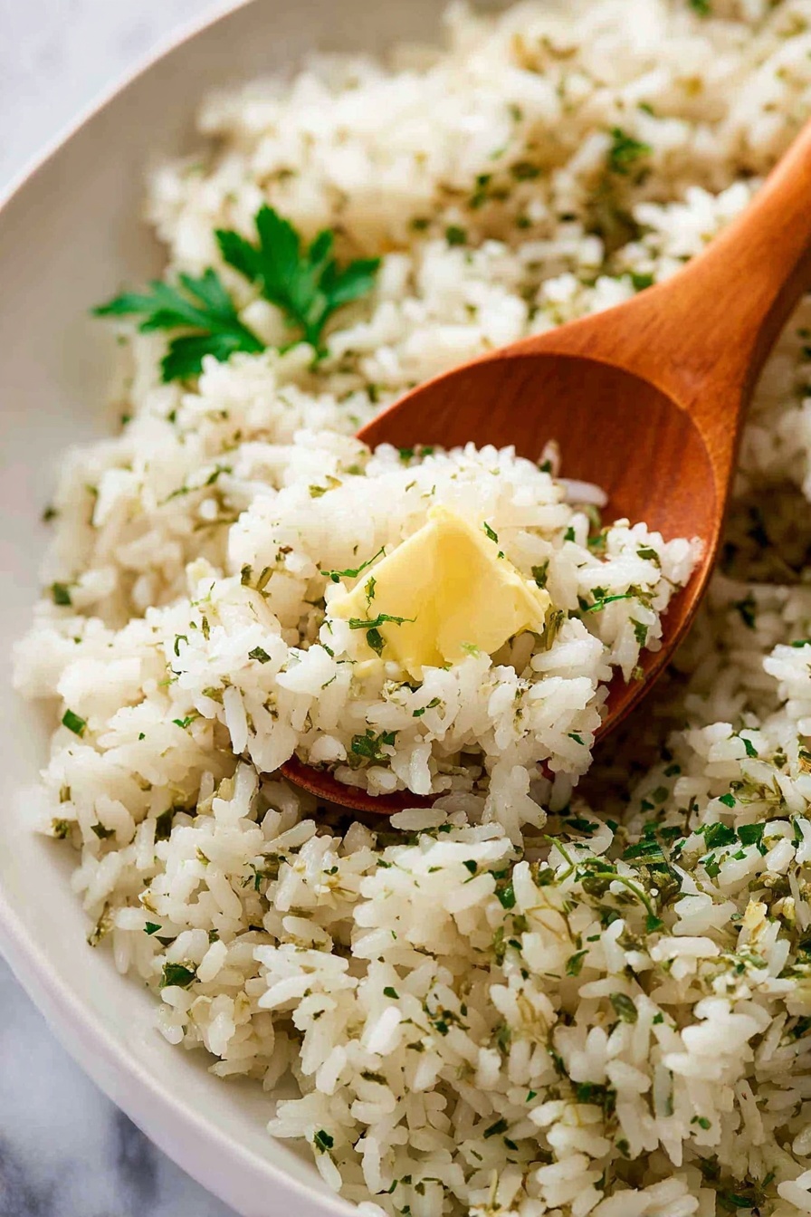 A white oval plate is full of cooked rice mixed with small green herb bits, making the rice look soft and fluffy. The rice has a light beige color with some darker specks of seasoning spread all over. On top, small green chopped parsley pieces are scattered, giving a fresh touch. There is a small dollop of light yellow butter melting into the rice near the center. A wooden spoon lies on the right side of the plate, partly under the rice. The background is a white marbled surface with a soft green and white cloth blurred in the back. Photo taken with an iphone --ar 2:3 --v 7