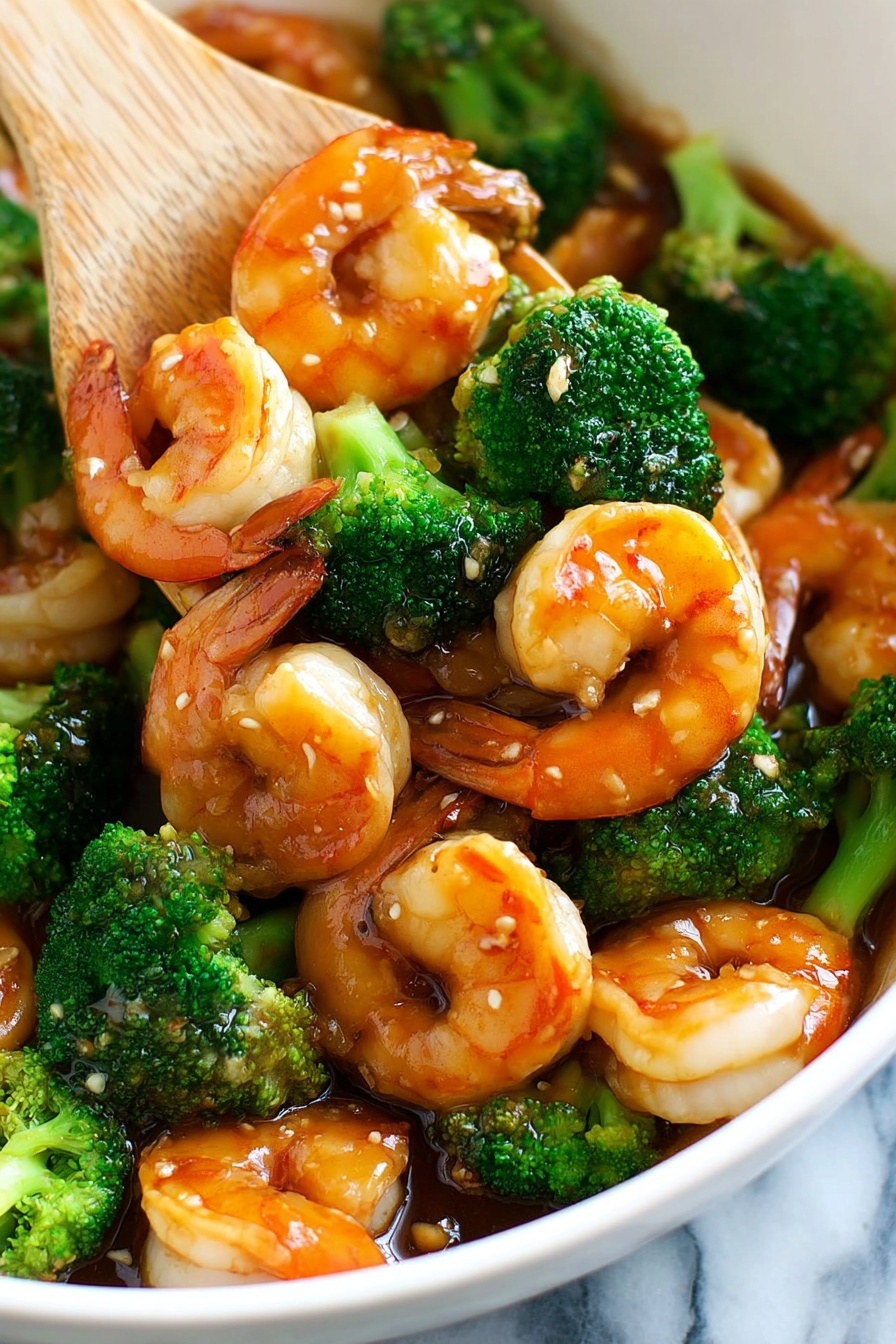 The dish shows a white bowl full of cooked shrimp and broccoli. There are about two layers: the bottom layer is bright green broccoli florets that look slightly steamed, and the top layer has plump shrimp with a shiny orange-pink shell and white flesh, coated with a glossy brown sauce with bits of garlic visible. A wooden spatula lifts a few shrimp from the bowl. The background is a white marbled texture. Photo taken with an iphone --ar 2:3 --v 7