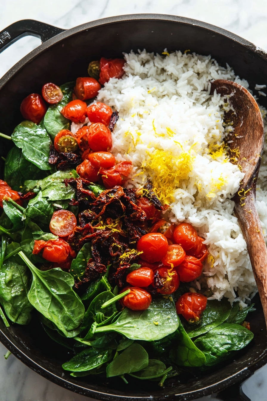 The image shows a black pan with layers of food inside. At the bottom, there is a base of fresh green spinach leaves, scattered with juicy red grape tomatoes, some whole and some cut in half. Above the greens lies a mound of soft, fluffy white rice. On top of the rice, bright red grape tomatoes are placed, both whole and halved, mixed with bits of dark, wrinkly sun-dried tomatoes and small yellow zest shreds, likely lemon. A wooden spoon is resting inside the pan, partially touching the ingredients. The pan is placed on a white marbled surface. Photo taken with an iphone --ar 2:3 --v 7
