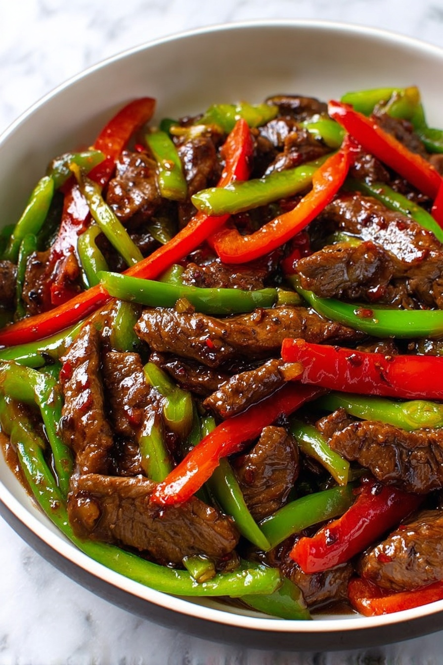 A close-up of a white bowl filled with slices of dark brown beef covered in a shiny sauce, mixed with thin strips of bright red and green bell peppers. The beef pieces have a slightly textured surface and are arranged evenly throughout the bowl, with the colorful peppers adding contrast. The sauce coats all ingredients, giving a glossy look that reflects light. The background shows a white marbled surface. photo taken with an iphone --ar 2:3 --v 7