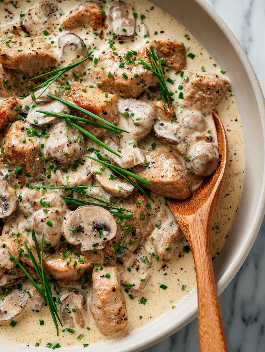A close-up view of several brown meat pieces in a creamy light brown sauce with visible tiny dark specks. Mixed in are light tan mushroom slices with soft edges, scattered evenly throughout the sauce. Green chopped herbs are sprinkled on top, adding pops of fresh color. A wooden spoon with a smooth, natural texture is partially submerged on the right side, resting among the sauce and ingredients. The dish is in a black pan, with a white marbled surface barely visible at the edges. photo taken with an iphone --ar 2:3 --v 7