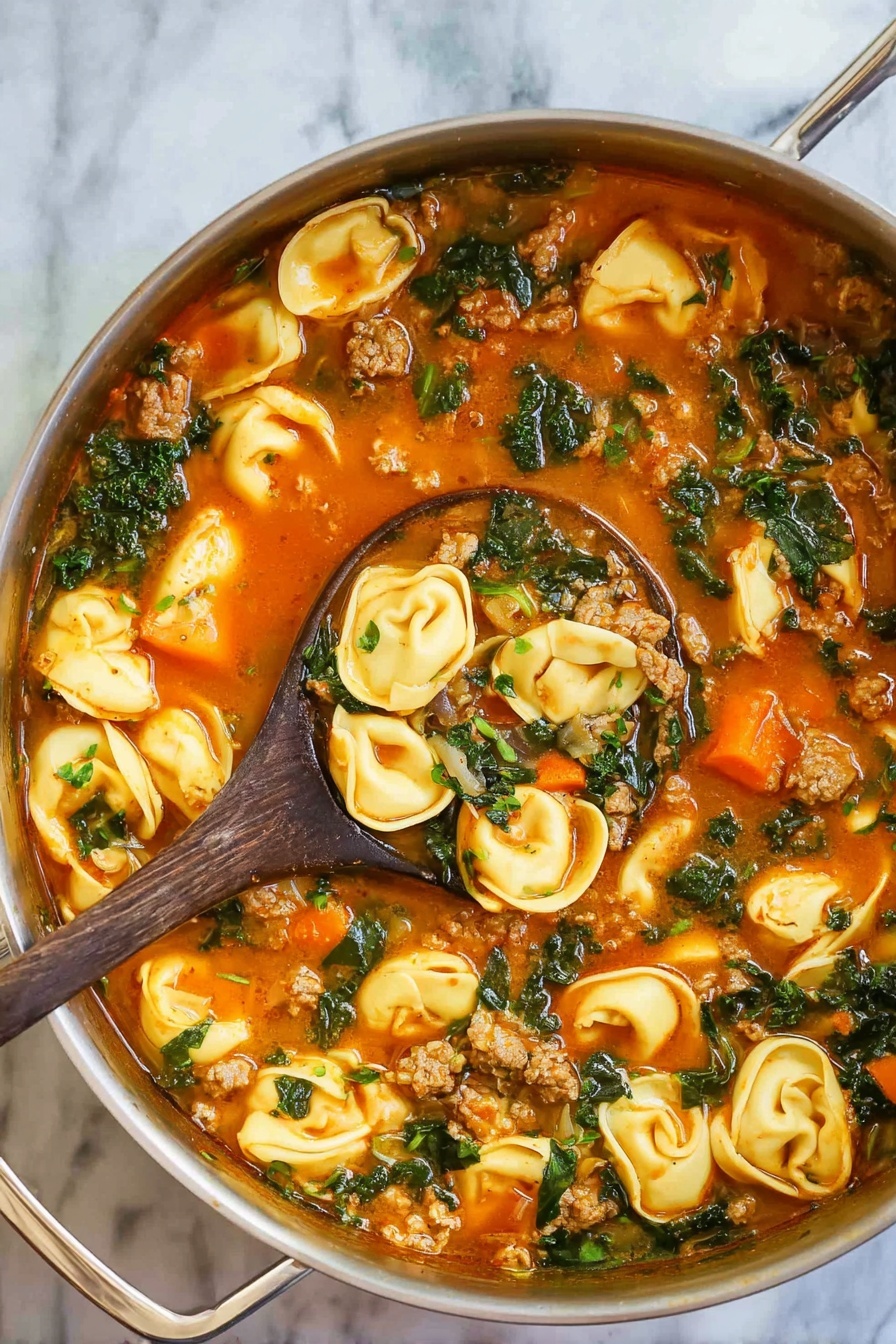 The image shows a silver pot filled with a warm soup. The soup has three main parts: golden-yellow tortellini pasta floating on top, small bits of light brown ground meat scattered throughout, and dark green leafy vegetables mixed in. The broth is light reddish-orange with visible herbs and small bubbles on the surface. A wooden spoon with a light wood color is dipping into the soup from the bottom right side. The pot rests on a white marbled surface. photo taken with an iphone --ar 2:3 --v 7