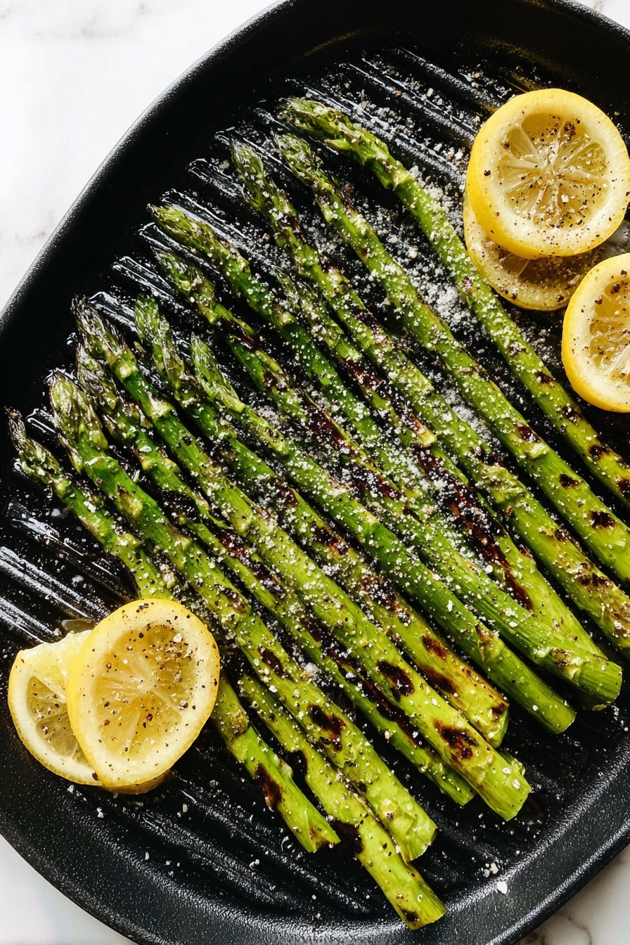 A black round grill pan filled with one layer of grilled green asparagus spears, arranged closely side by side with visible char marks and a sprinkling of coarse salt on top. Three lemon wedges with slight grill marks rest on the right and bottom edges of the pan. The pan sits on a white marbled surface. Photo taken with an iphone --ar 2:3 --v 7