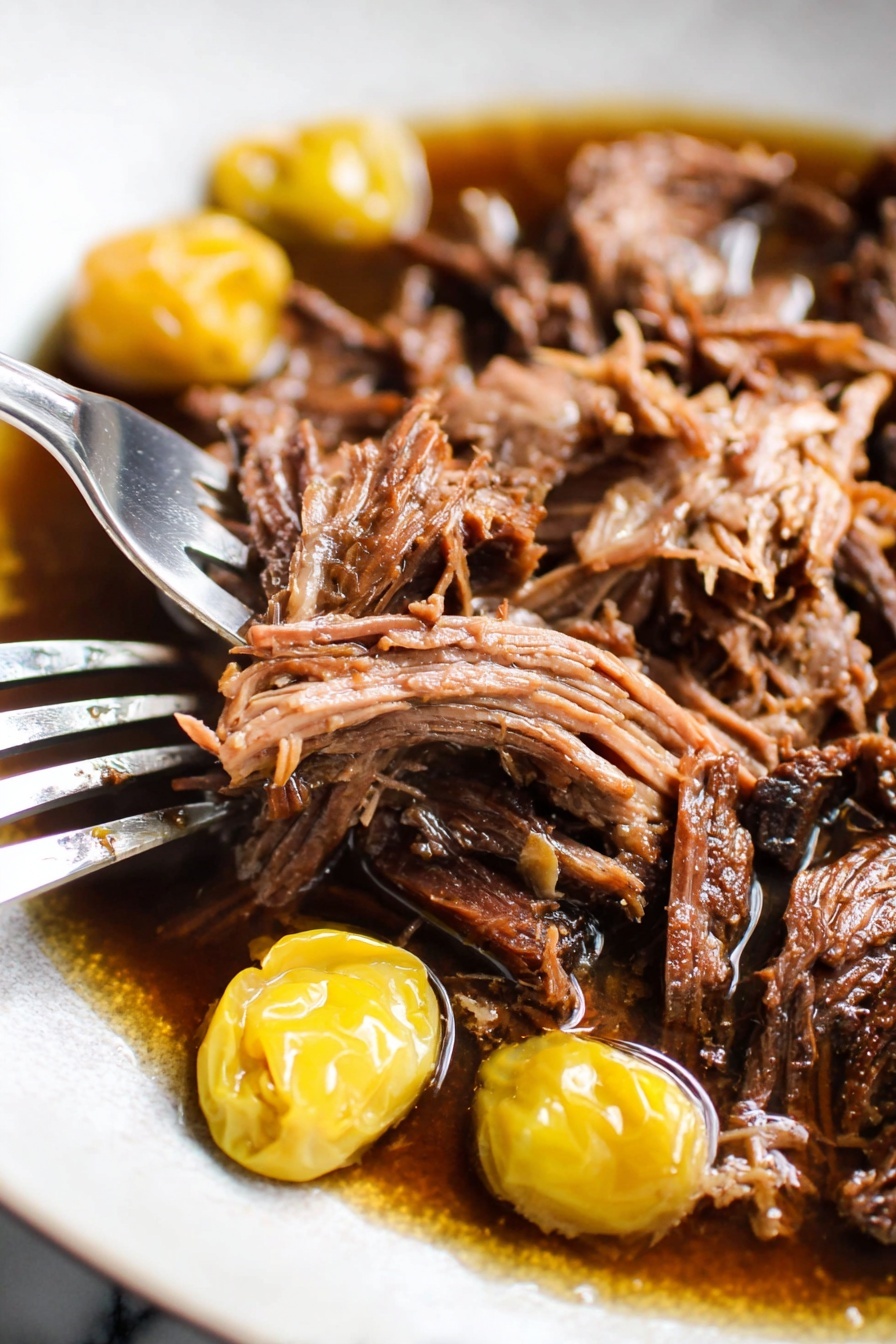 The image shows a white plate with two main layers of food. The bottom layer is a smooth, creamy white mash, likely mashed potatoes, spread in a circle across the plate. On top of this is a heap of shredded dark brown meat, which looks tender and juicy, with some juice pooling around it. Two whole yellow pickled peppers rest on the meat, adding a pop of bright color. Small green herb pieces are sprinkled over the dish for garnish. A knife with a wooden handle rests on the edge of the plate. The plate is set on a white marbled texture surface with scattered fresh herbs and a light pink cloth nearby. Photo taken with an iphone --ar 2:3 --v 7