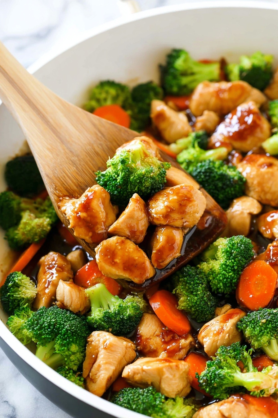 A white pan filled with cooked chicken pieces and bright green broccoli florets, both covered in a shiny brown sauce. There are also a few soft orange carrot slices mixed in. A wooden spatula is scooping up some pieces from the pan, showing the glossy texture of the sauce on the chicken and vegetables. The pan sits on a white marbled surface. photo taken with an iphone --ar 2:3 --v 7